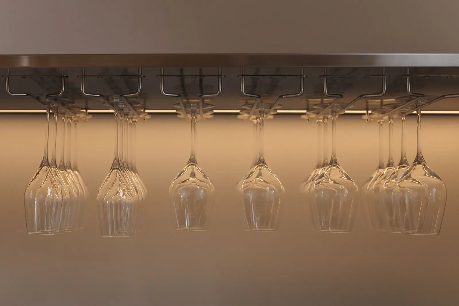 Wine glasses hanging upside down by their stems from a metal rack mounted under a cabinet