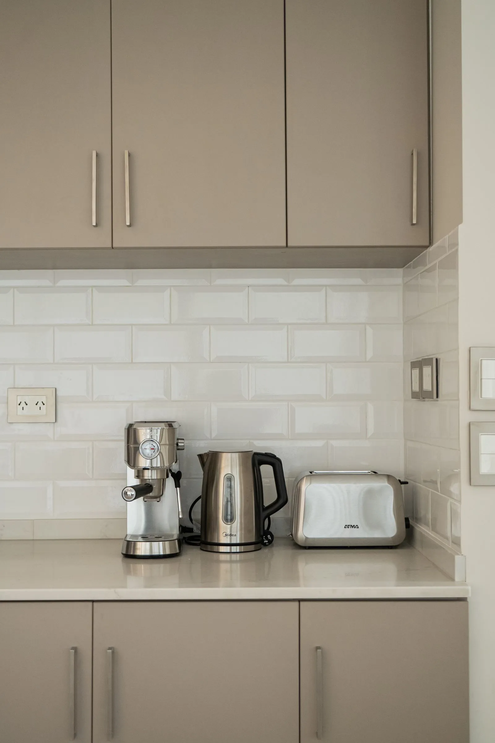 A coffee maker, kettle, and toaster lined up on a clean modern kitchen counter