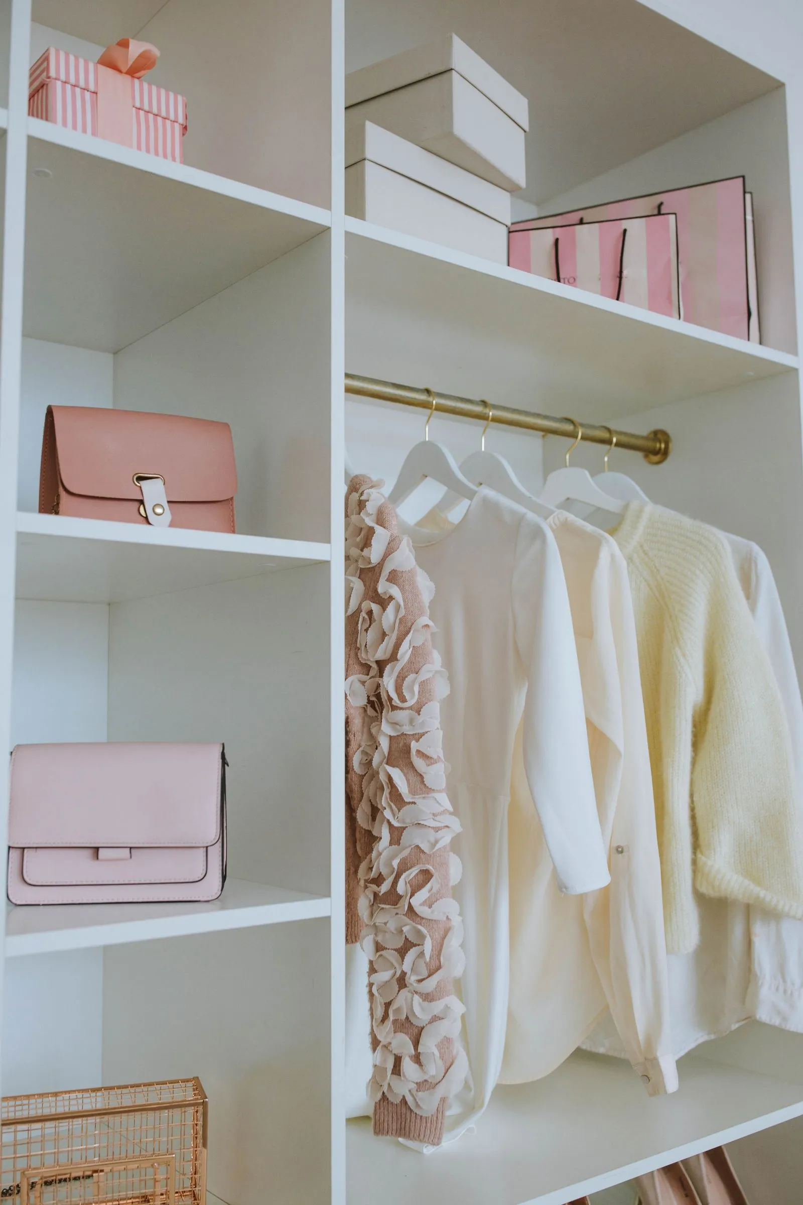 A closet shelving unit with individual cubbies holding handbags, next to a hanging rod of folded knits