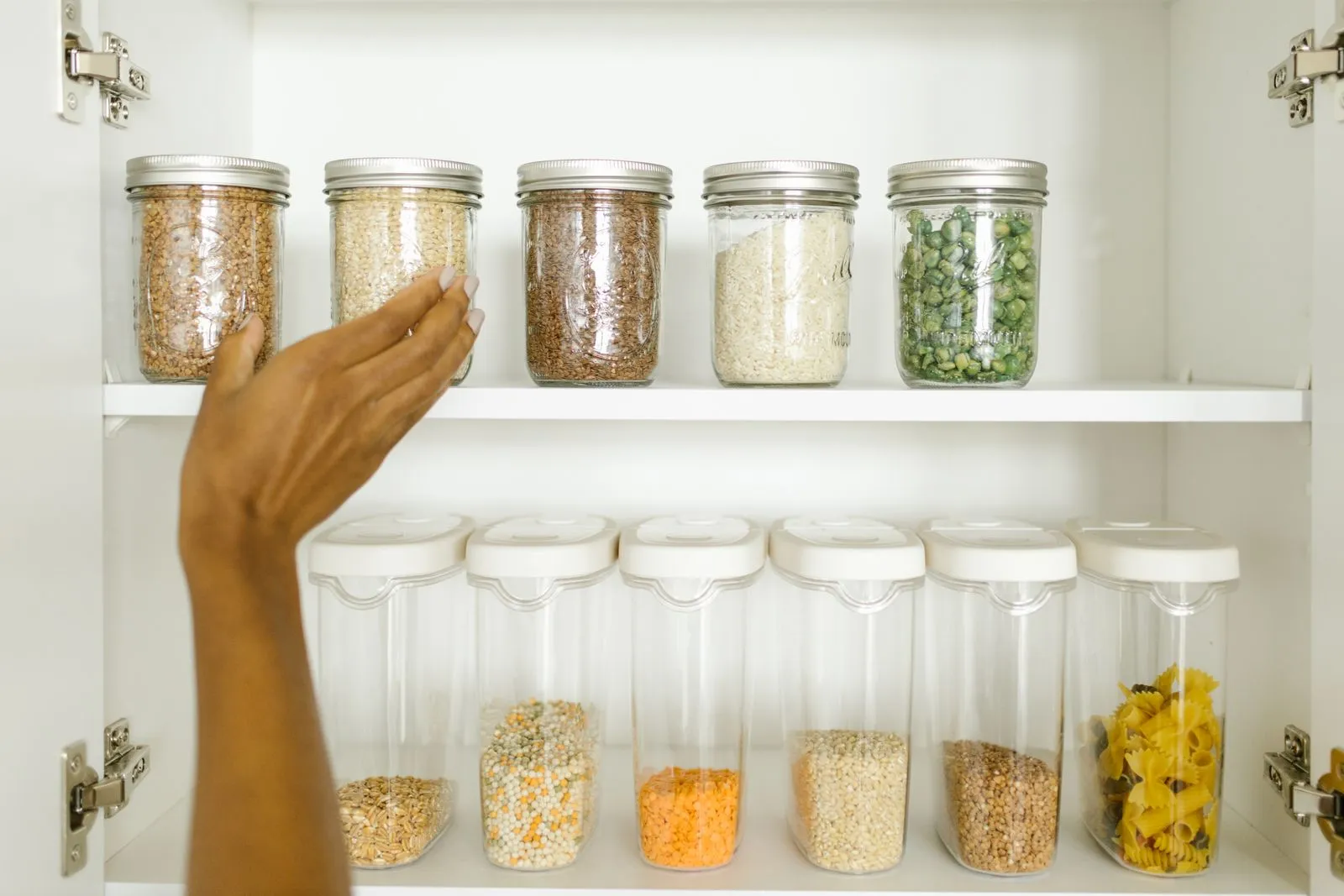 Neatly organized pantry shelf displaying labeled glass and plastic containers of grains and pasta