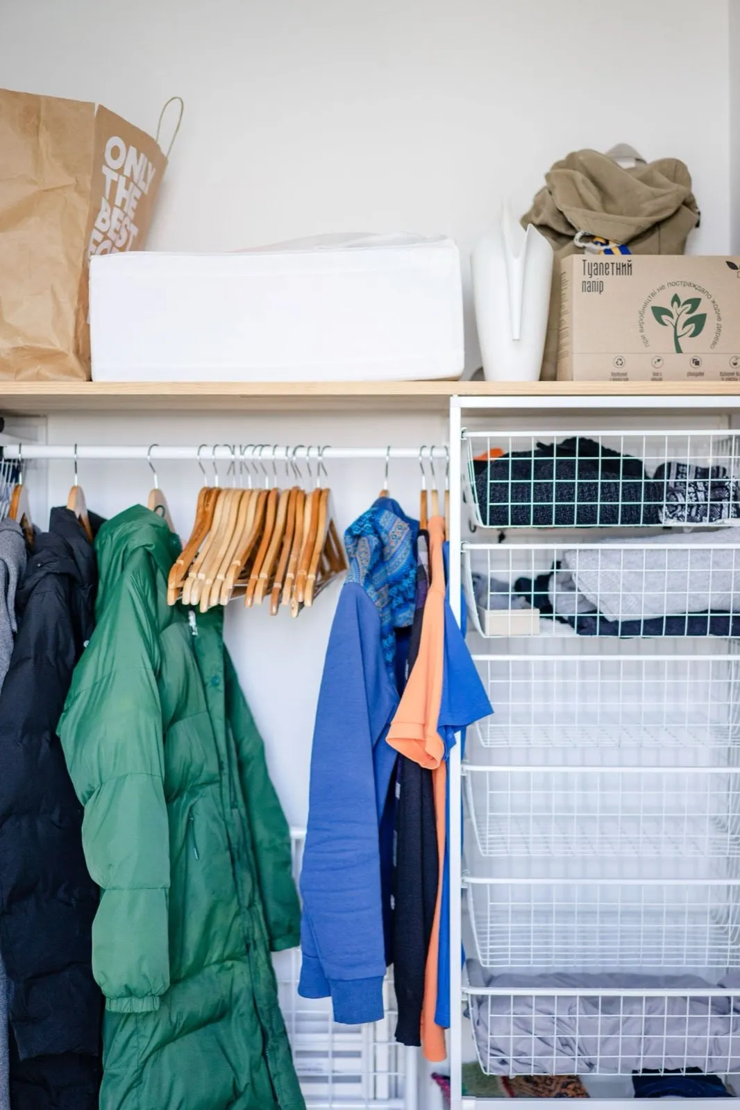 A closet rod of hanging coats next to a wire storage-basket unit stocked with folded clothes