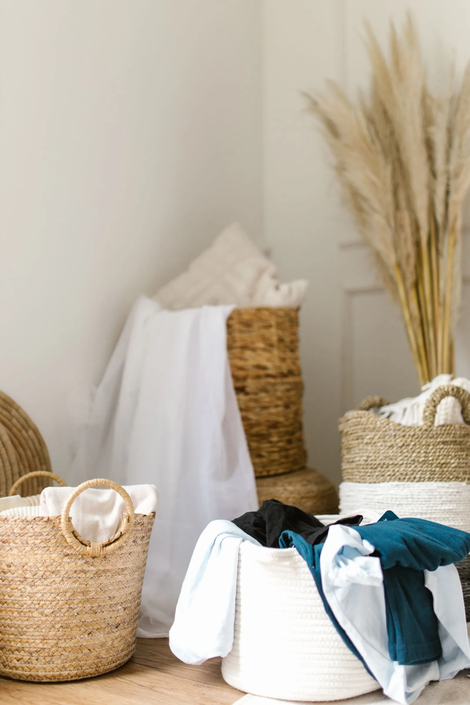 Woven and rope laundry baskets on a wooden floor, one holding folded white linens and another filled with teal and light blue clothes
