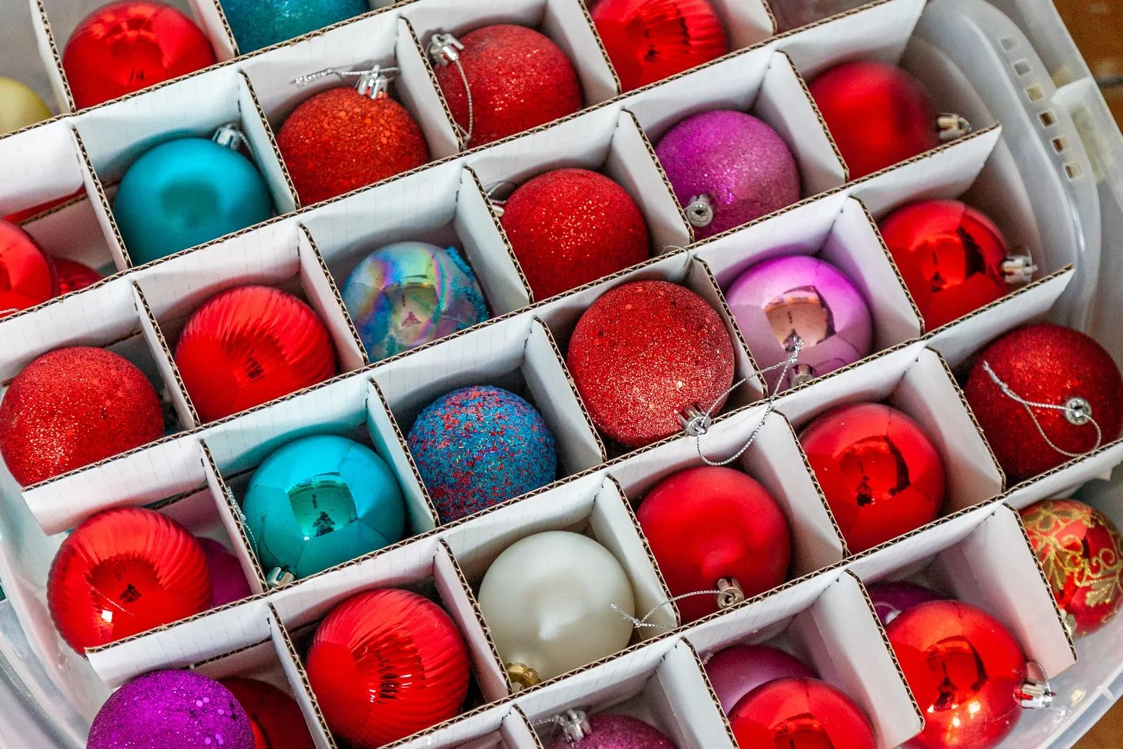Christmas ornaments organized in cardboard dividers inside a flat plastic storage bin, viewed from above