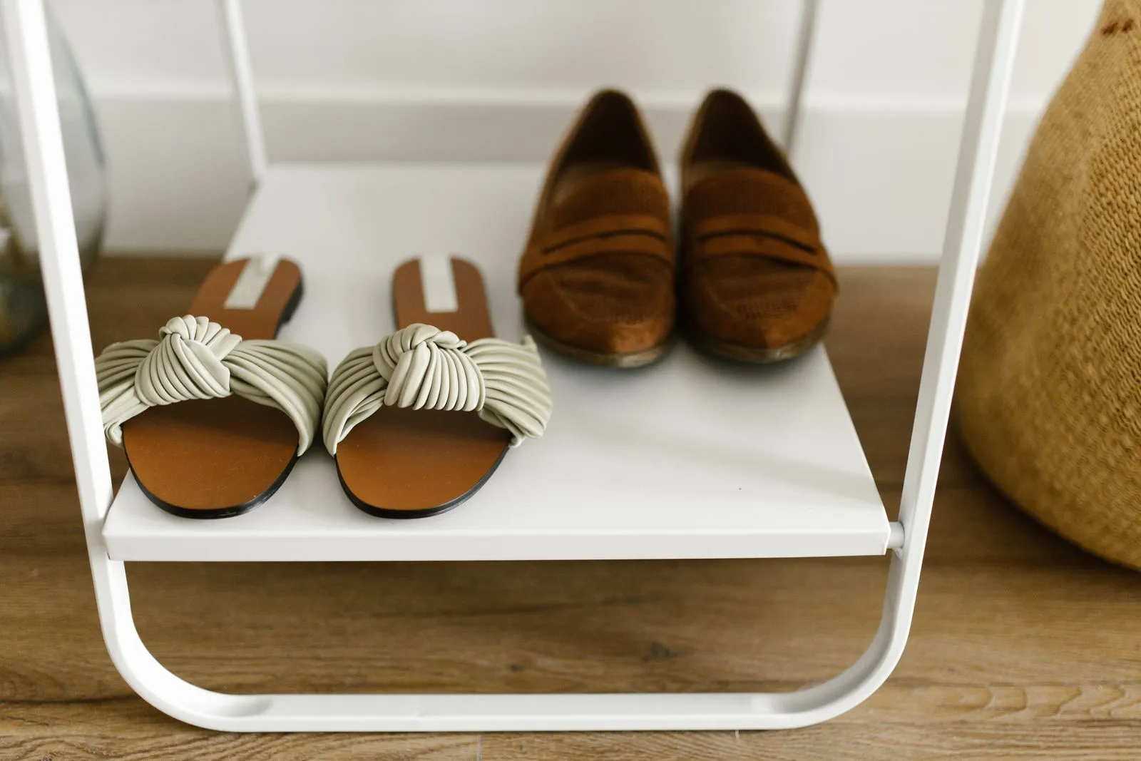 Close-up of stylish sandals and loafers arranged in pairs on a minimalist white shelf