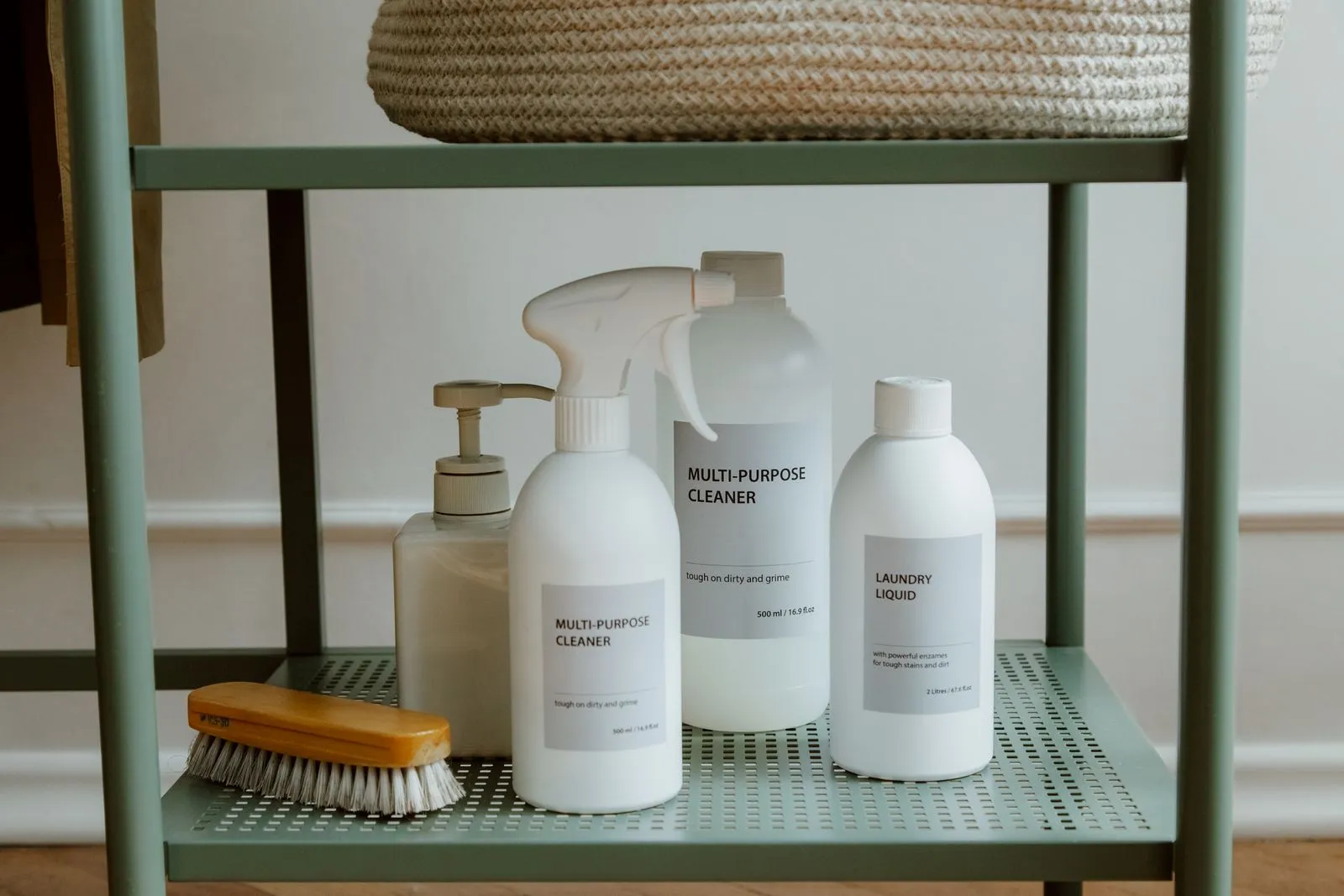 Multi-purpose cleaner, a pump soap bottle, laundry liquid, and a scrub brush lined up together on a shelf