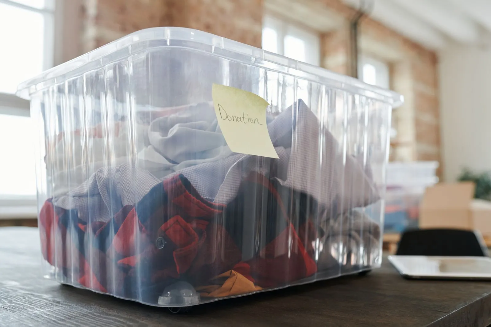 A clear plastic bin marked with a handwritten donation note, filled with shirts pulled during a closet cull