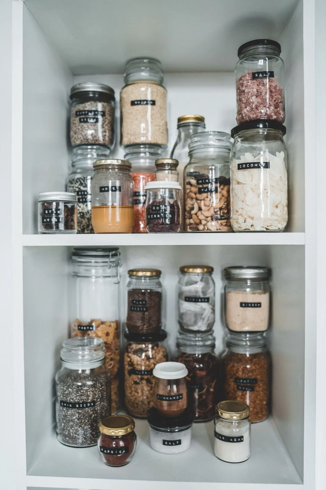 Individually labeled glass pantry jars holding spices, seeds, and dry goods
