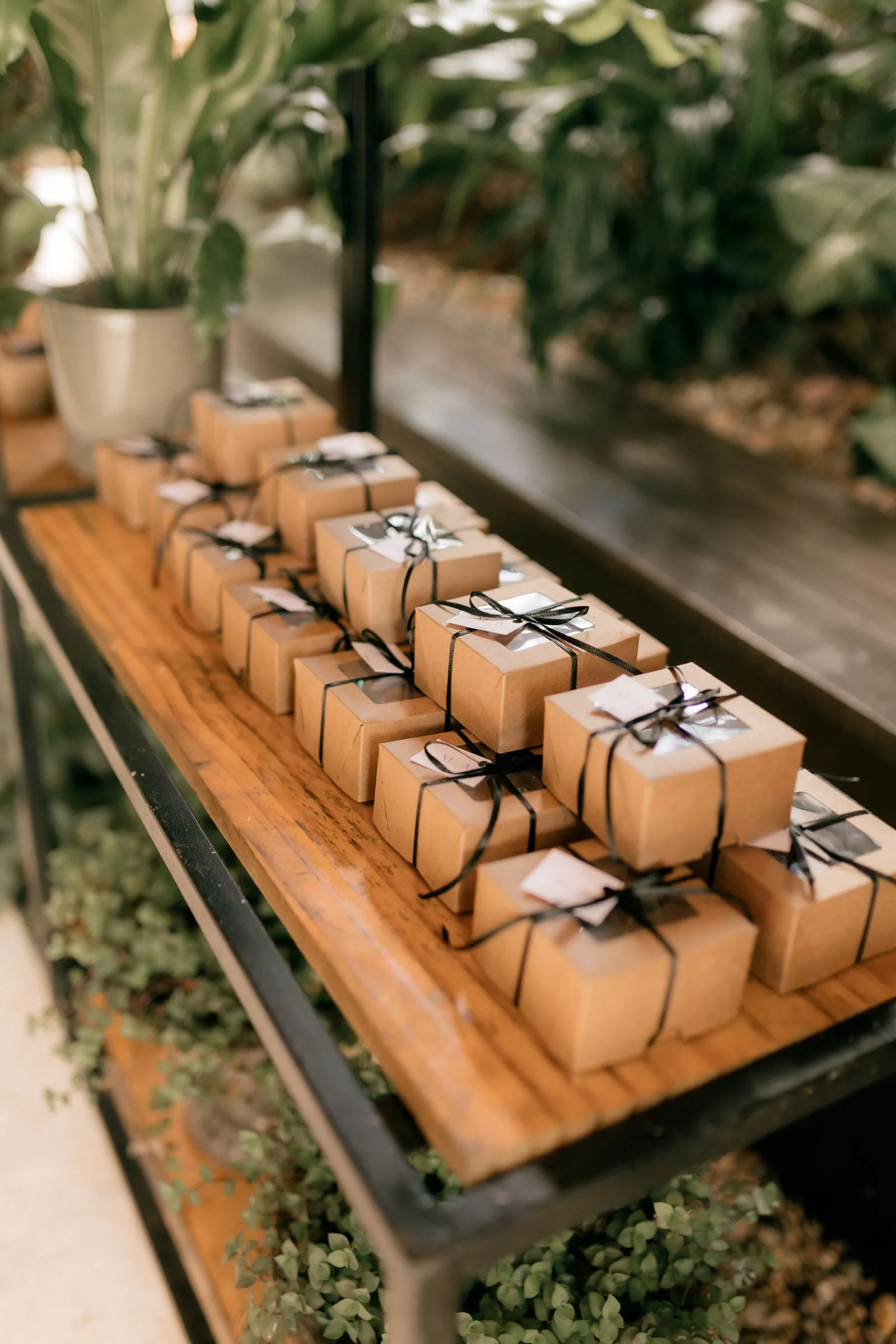Small kraft paper gift boxes tied with black ribbon and paper gift tags, arranged in neat rows on a wooden shelf