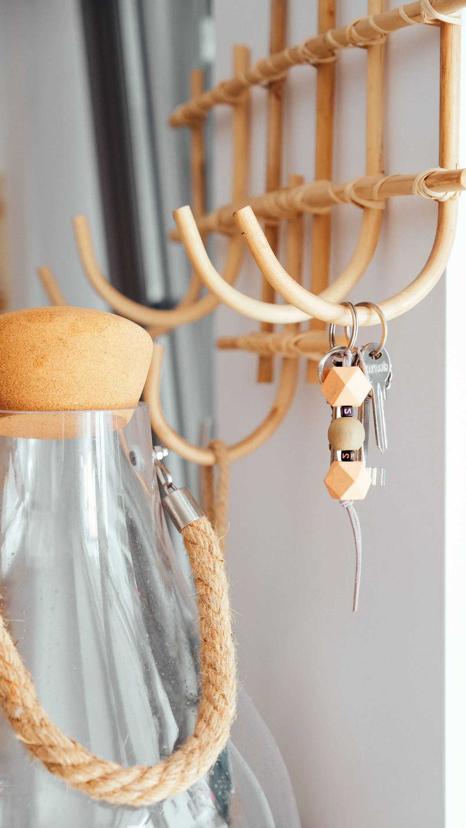 Close-up of woven rattan wall hooks holding a keychain and a set of keys next to a corked glass bottle