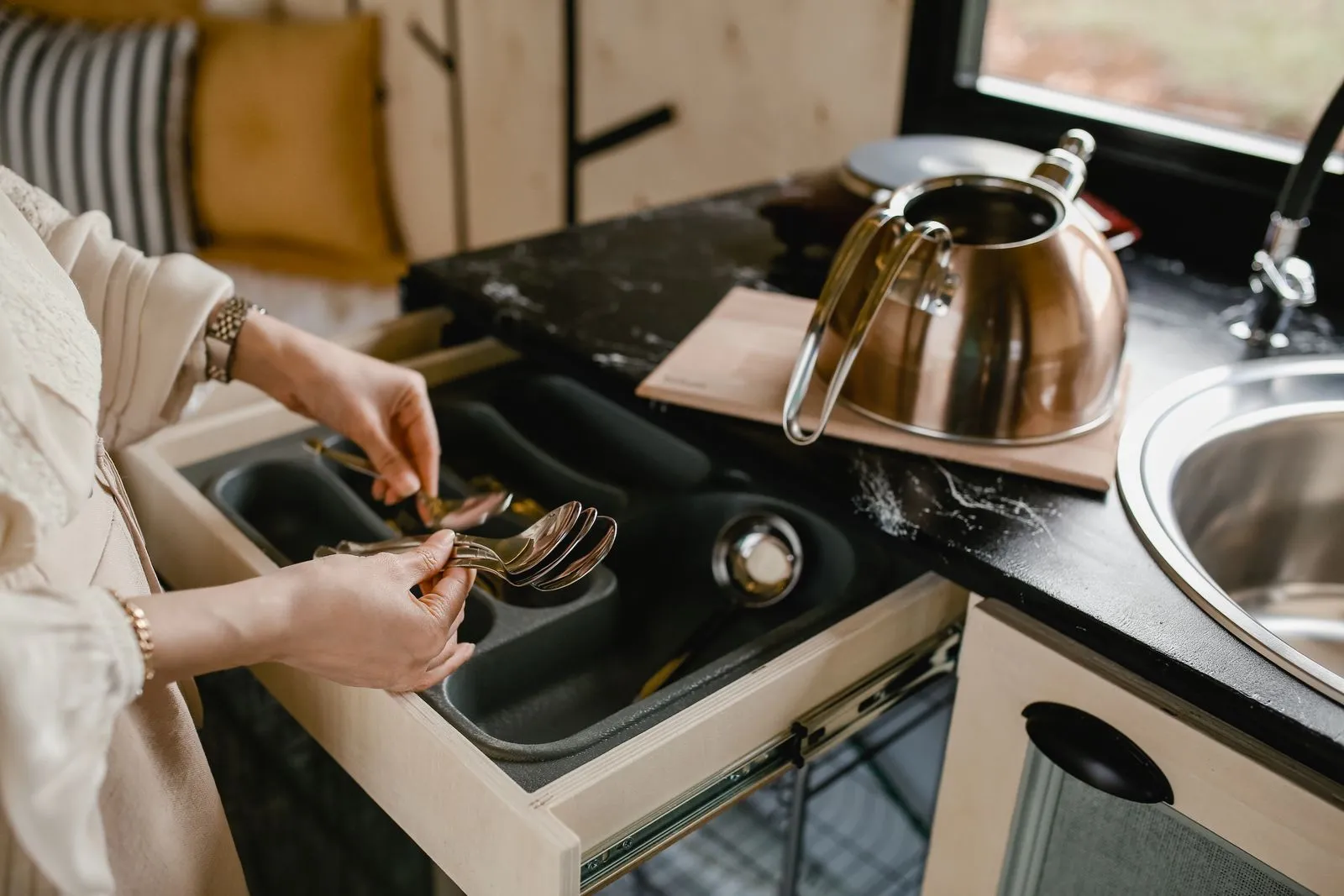 Hands placing forks into a compartmented cutlery tray inside an open kitchen drawer, sorting silverware into its zoned slots