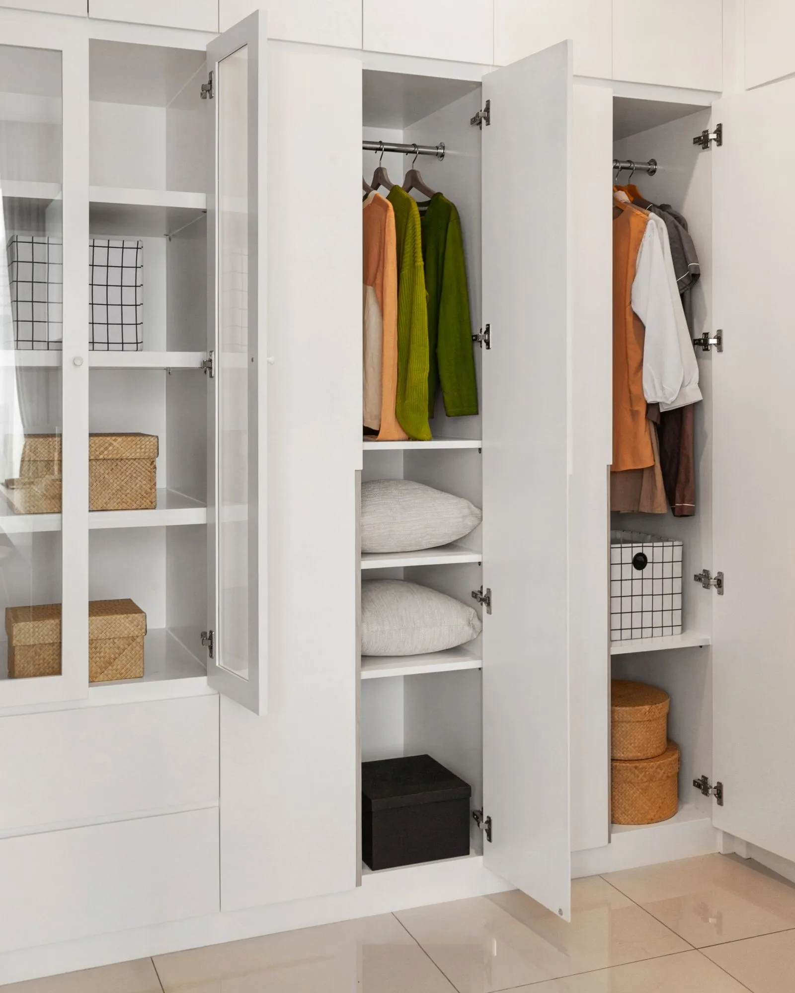 Open wardrobe closet rod holding hanging sweaters above built-in shelves storing folded pillows and storage boxes