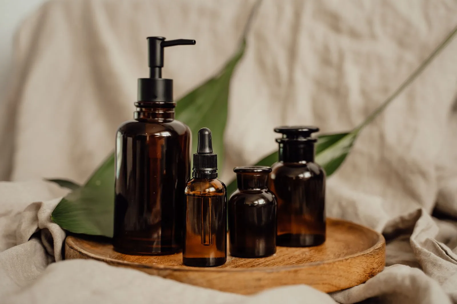 Amber glass dropper and pump bottles grouped together on a round wooden tray against a linen backdrop