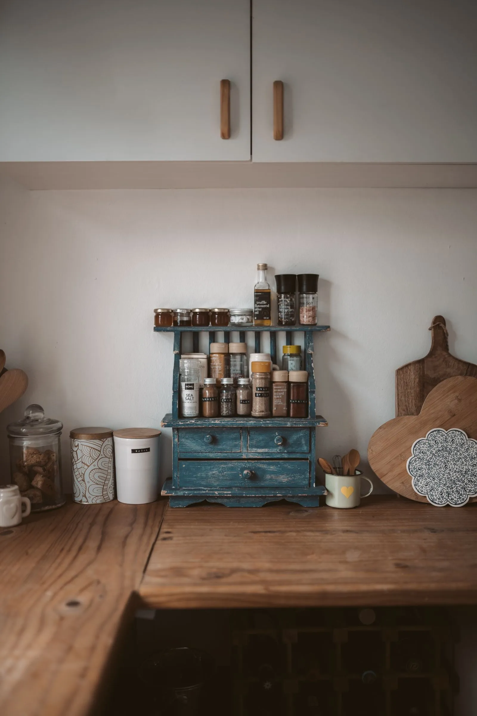 Small spice jars labeled turmeric, chia, flax, and mixed spice lined up on the tiered shelves of a wooden spice rack, each label facing forward