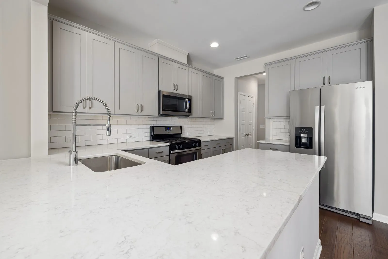Tidy kitchen with gray upper and lower cabinets, a white quartz counter, and a stainless steel refrigerator and microwave