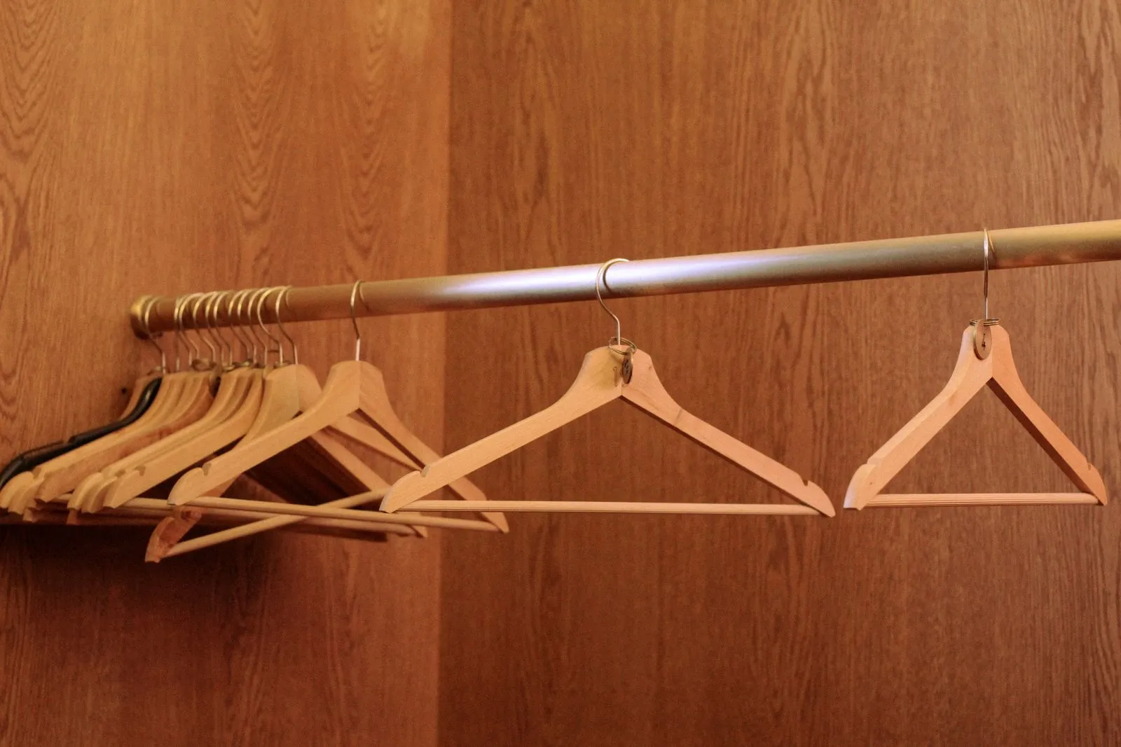 A row of wooden clothes hangers on a gold metal rod against a wood-paneled closet wall