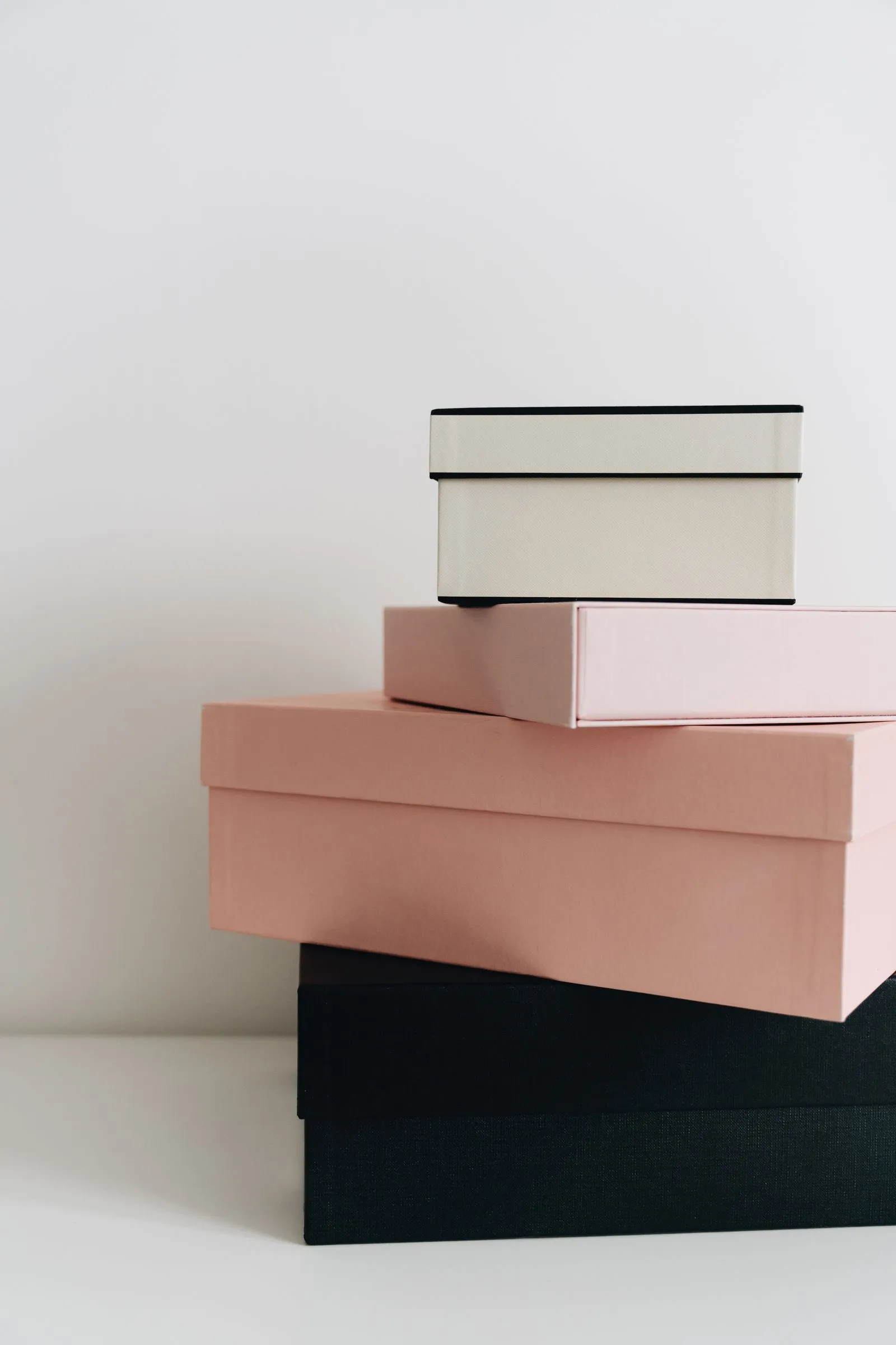Three flat storage boxes in cream, pink, and black stacked in a small, tidy pile