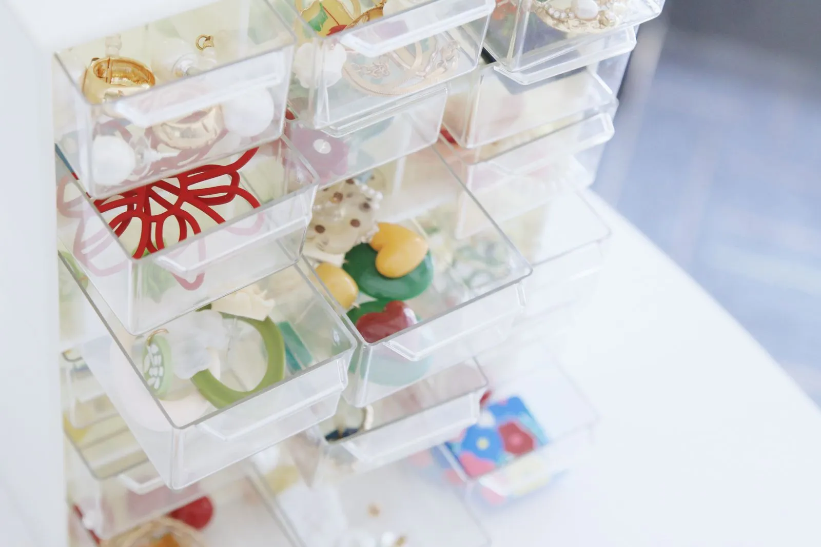 A clear divided jewelry organizer with small compartments holding rings, bracelets, and beads