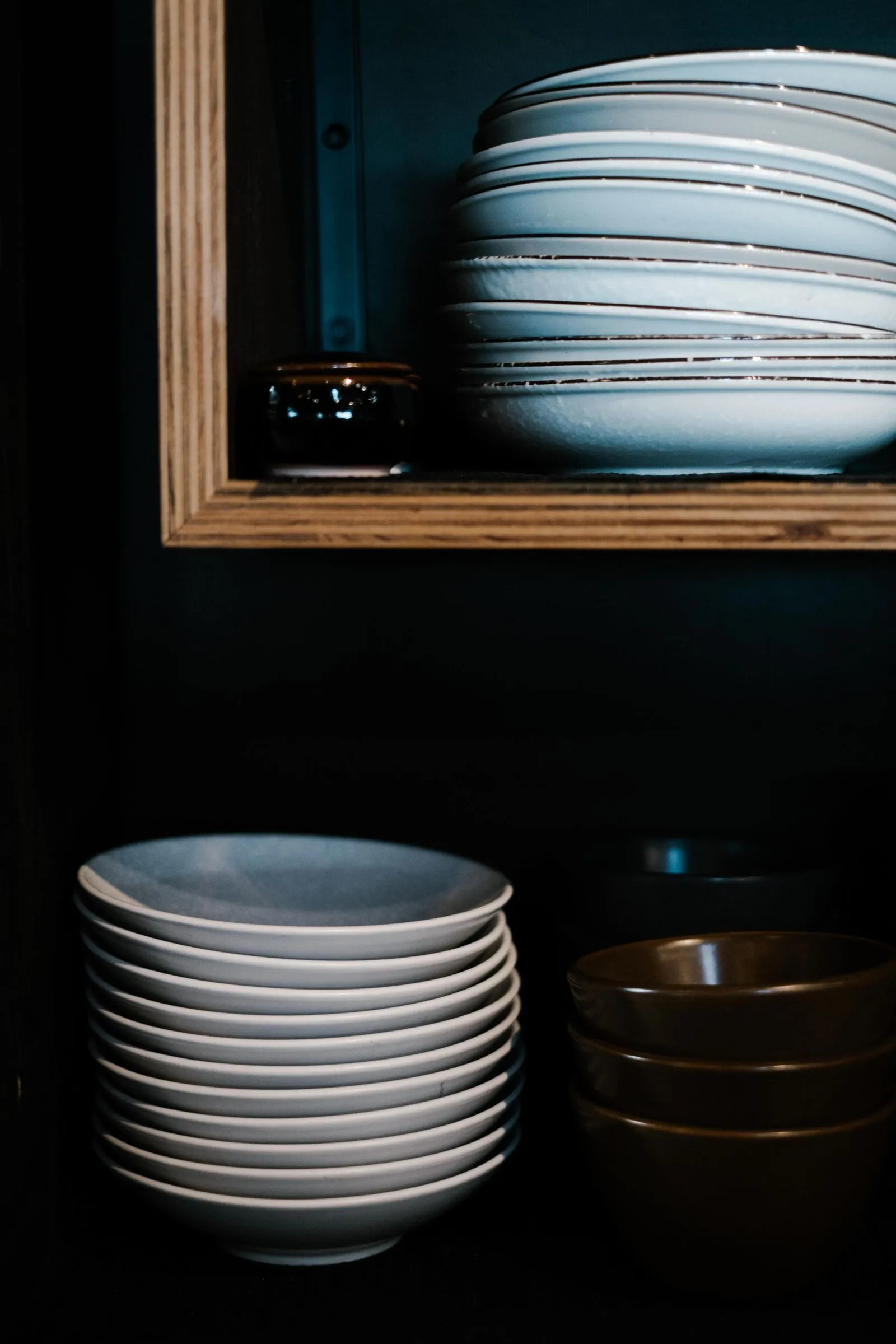 Stacked bowls and plates organized on separate shelves inside a wood-framed kitchen cabinet