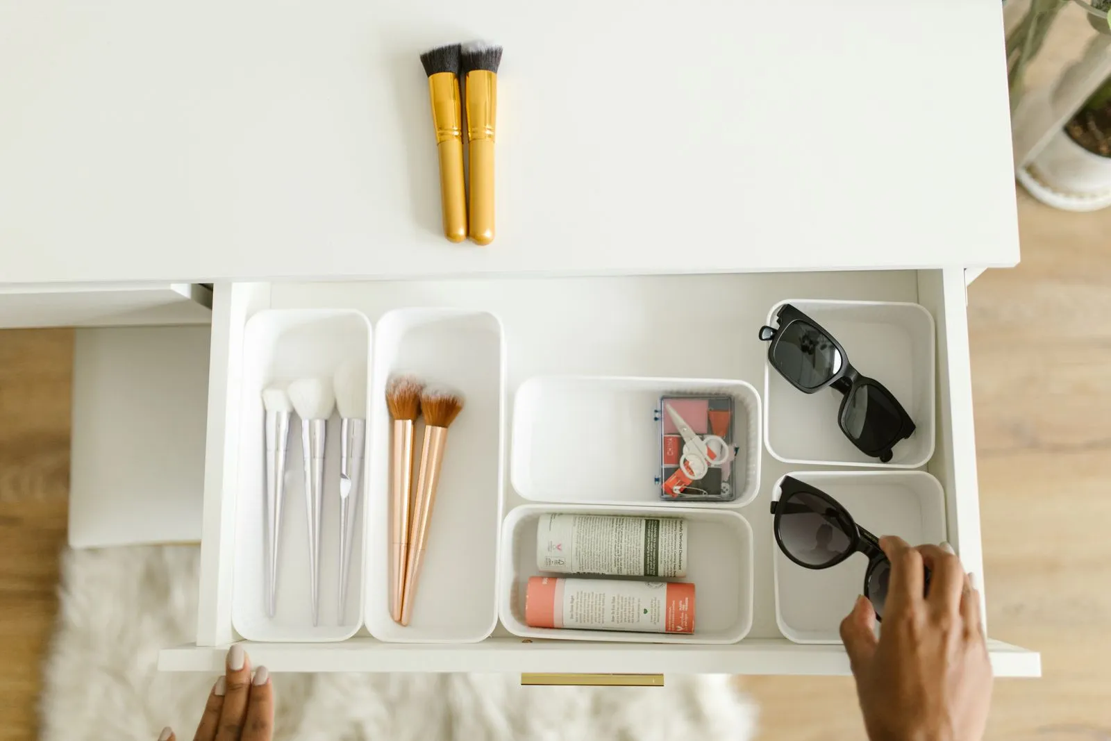 An open vanity drawer with divided compartments holding brushes, sunglasses, and small accessories