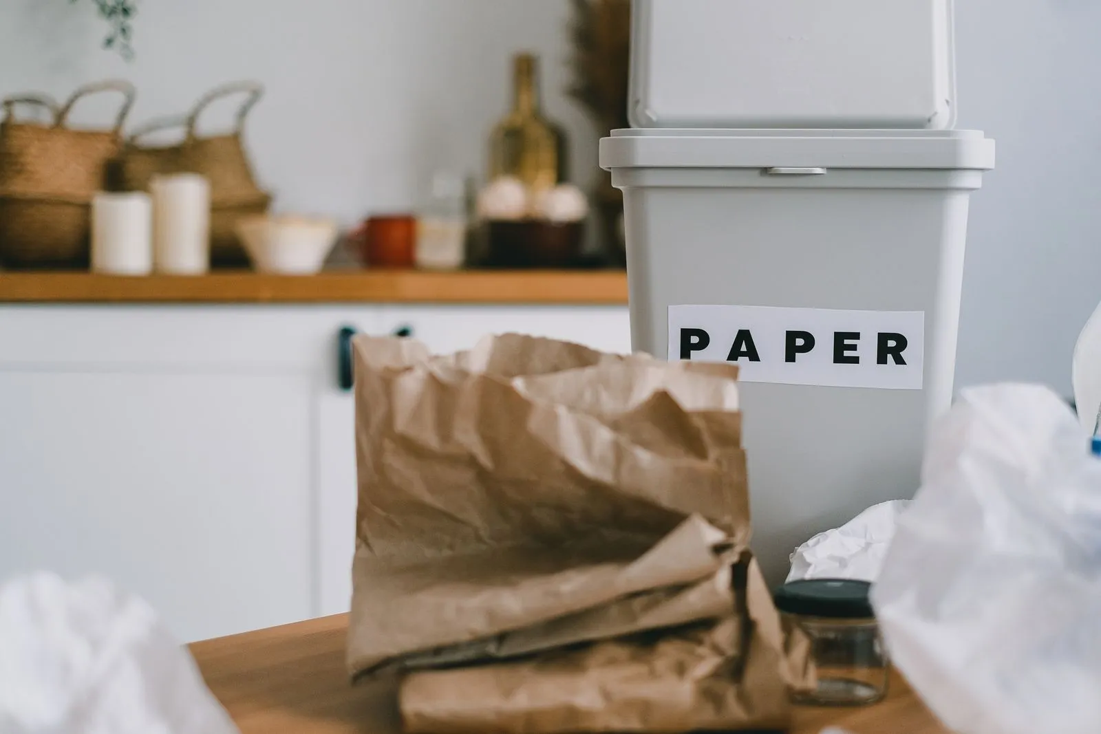 Slim bin labeled PAPER on a kitchen counter with paper bags stacked in front of it