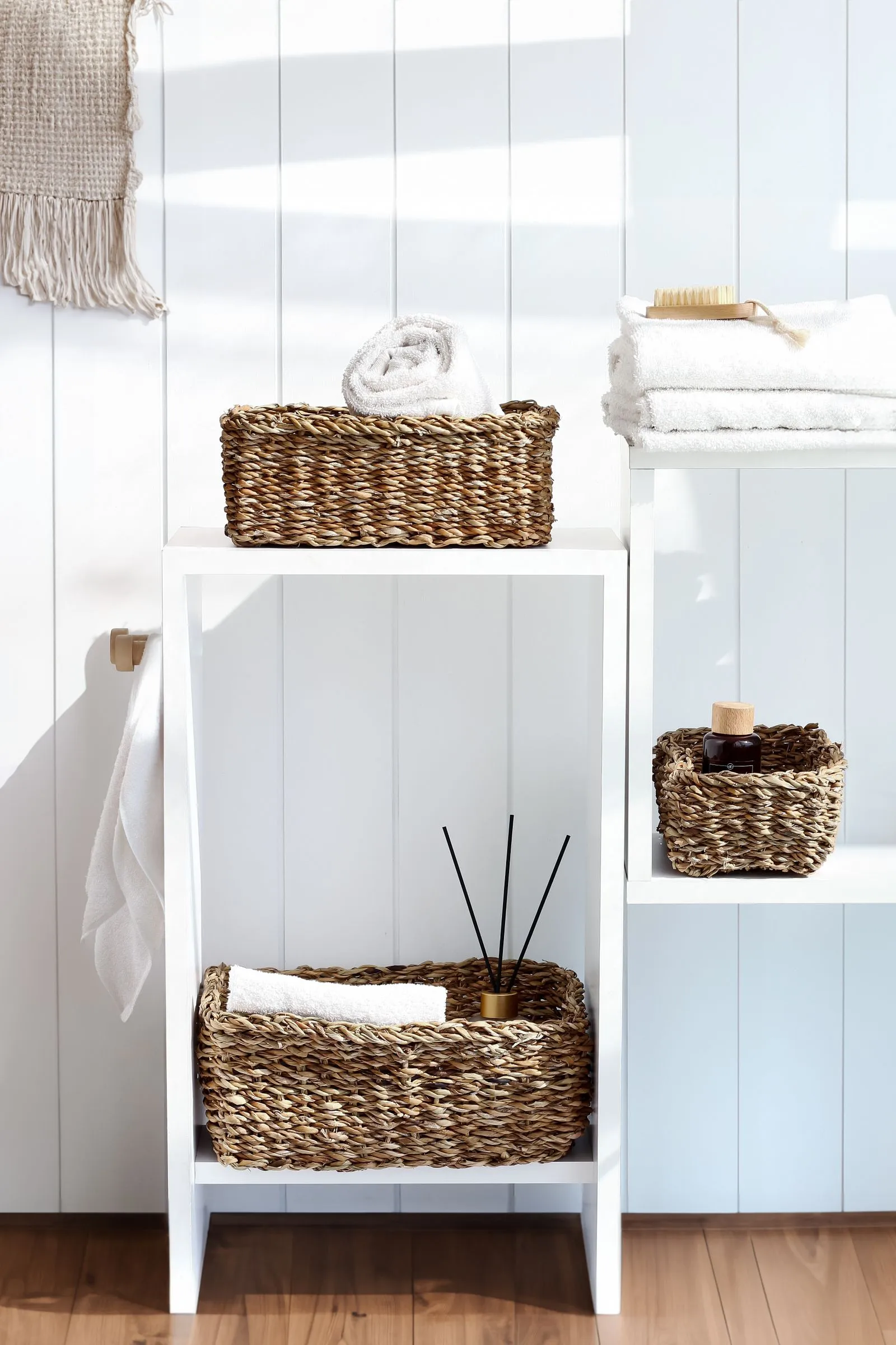 Woven baskets holding folded and rolled white towels on white bathroom shelving