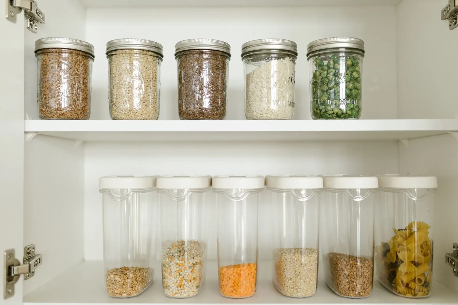 Mason jars of grains on a top shelf above a row of empty stackable canisters ready to be filled
