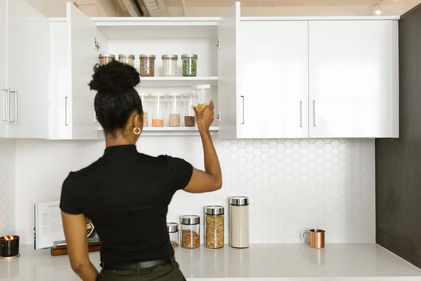 A woman organizing labeled glass food storage jars on a kitchen cabinet shelf