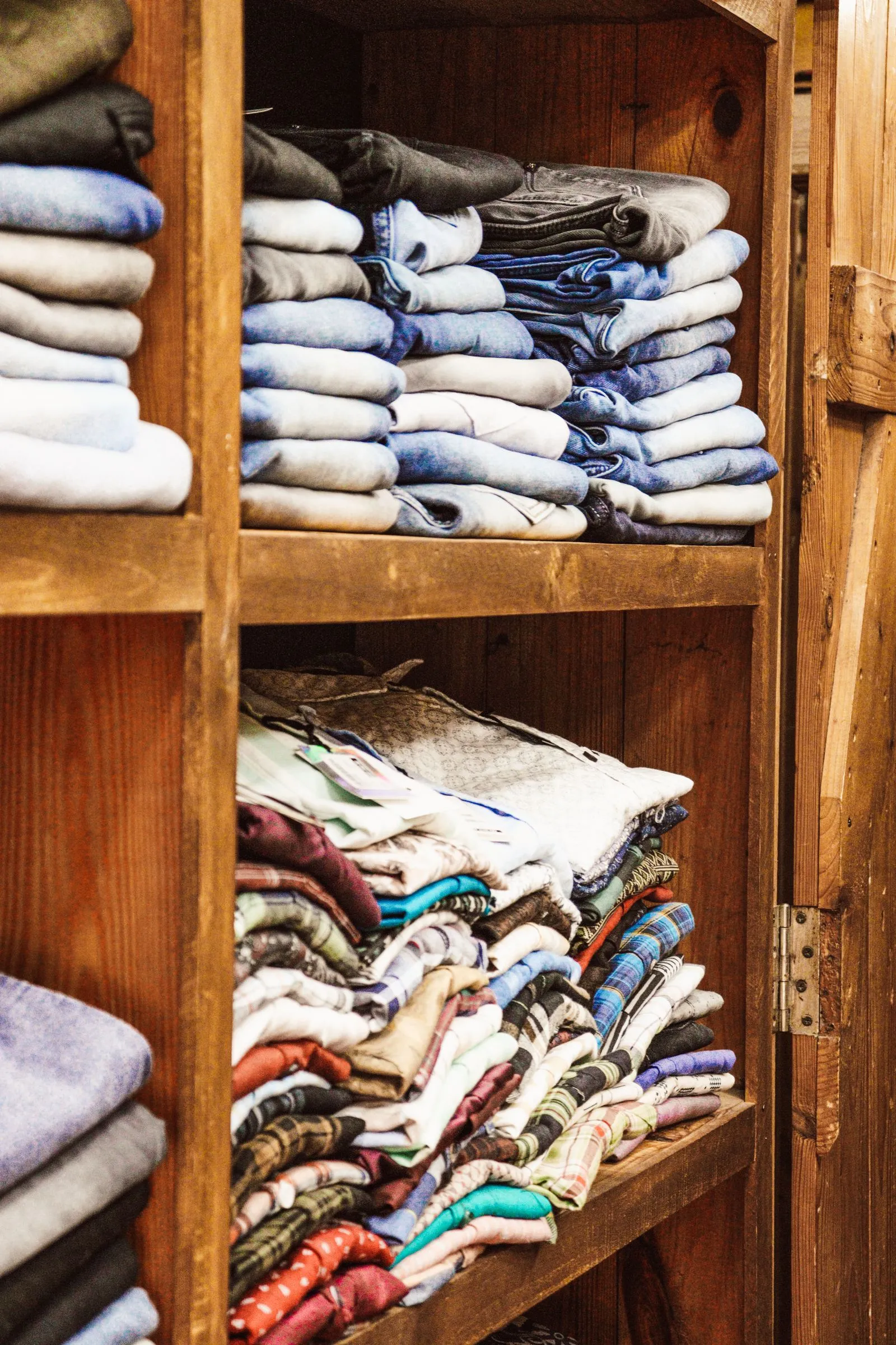 Wooden shelving with vertical dividers separating stacked folded jeans and shirts by color