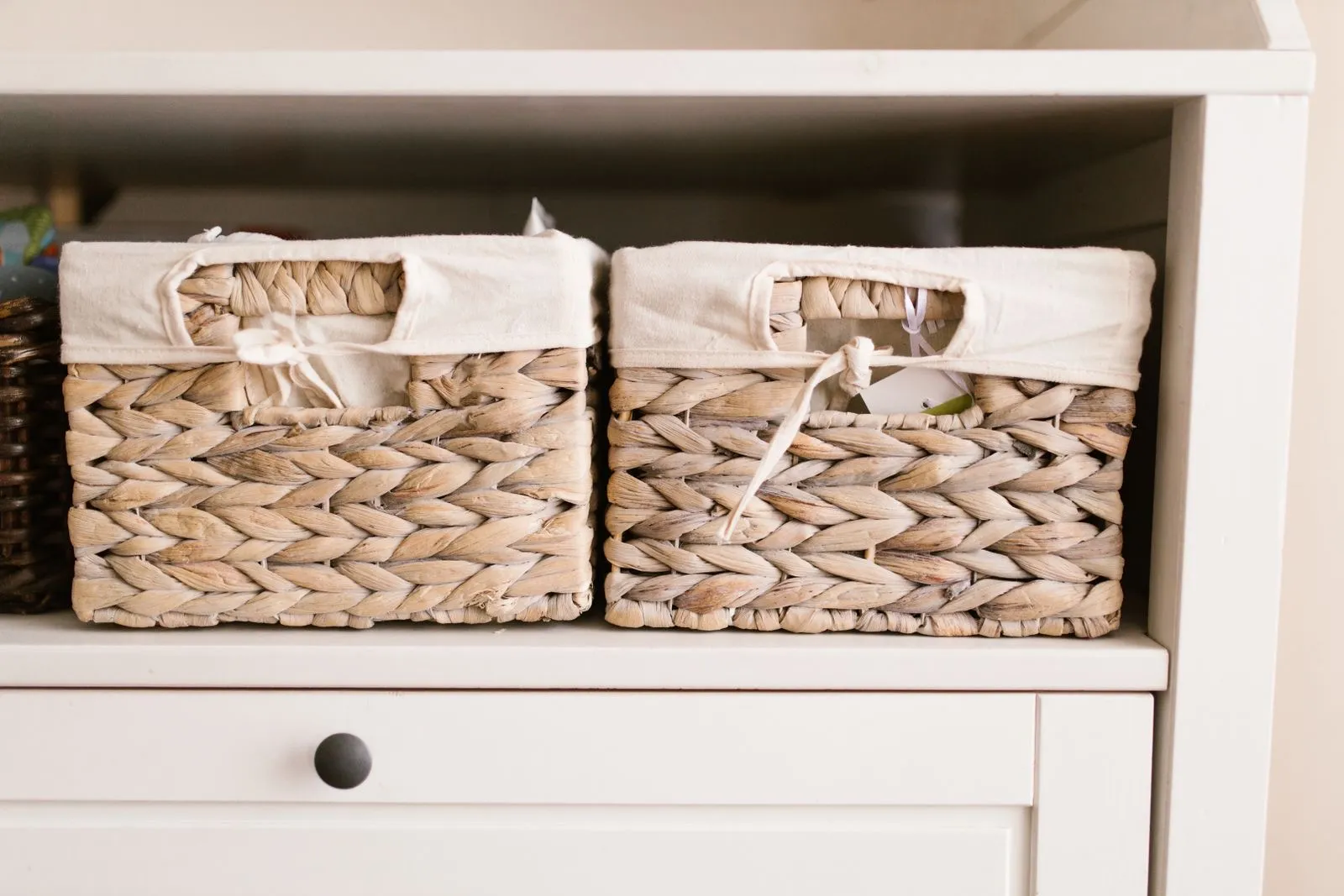 Two fabric-lined woven storage baskets sitting side by side on a white shelf